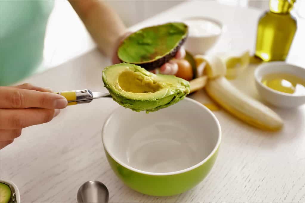 Making avocado hair mask. Scoop out avocado plup and add olive oil and honey. 
